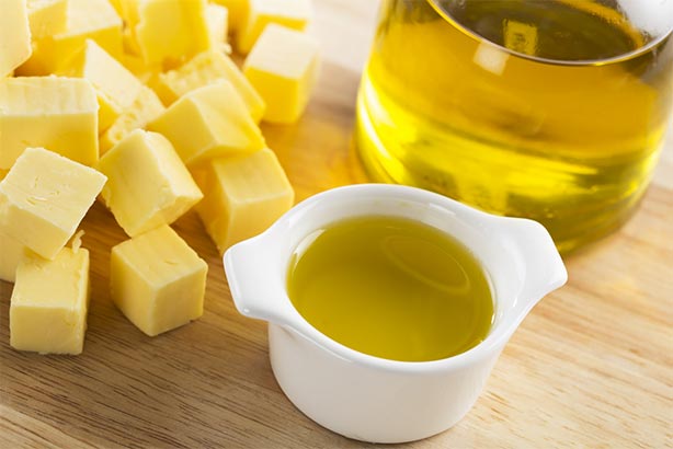 Cubed butter and liquid butter oil in a container on a wooden cutting board